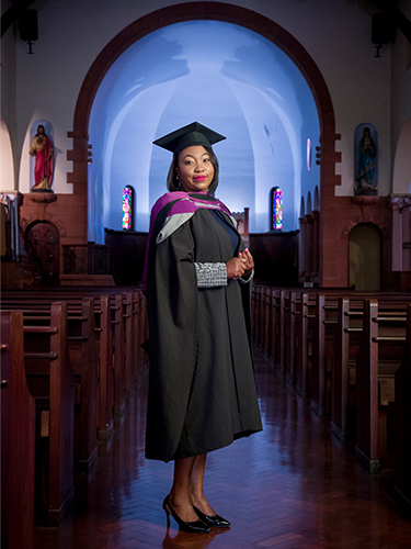 Bolanle Enang who graduated with a master's from UP's Faculty of Theology stands in a church in her graduation cap and gown.