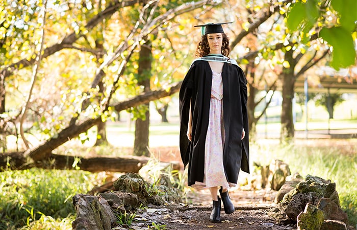 UP graduate Mia Gerber standing in the middle of an autumn garden path in her graduation gown and cap.