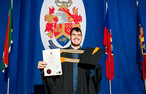 UP student Rudolph Boraine in a graduation gown holding his certificate and graduation cap.