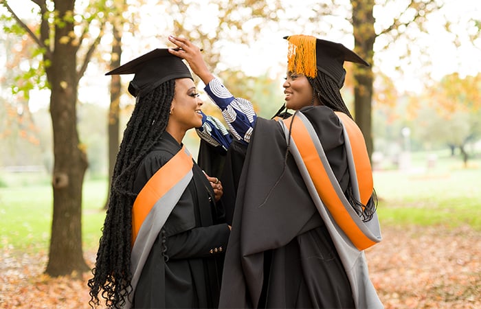 Current UP Student Representative Council president Thuto Mashile and former SRC president Lerato Ndlovu smile at each other in a garden in their graduation caps and gowns.