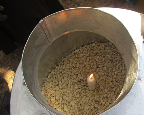 A lit candle in a metal silo filled with dried maize