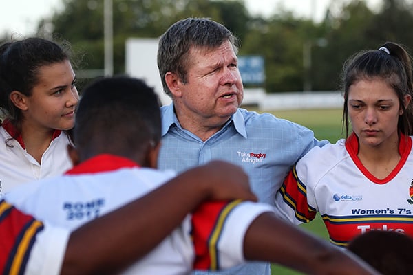 Delta Drone TuksWomensRugby 7s coach Riaan van der Merwe and some of his players stand in a circle with their arms on each other's shoulders.