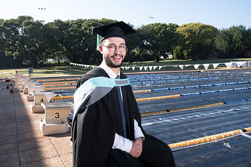 UP engineering graduate Chase Onorati sits poolsode on a diving platform dressed in a graduation gown and cap