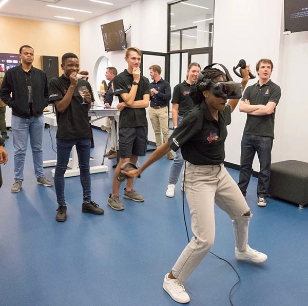 A student dressed in grey jeans and a black t-shirt animatedly uses plays on a XR Toybox while other students look on