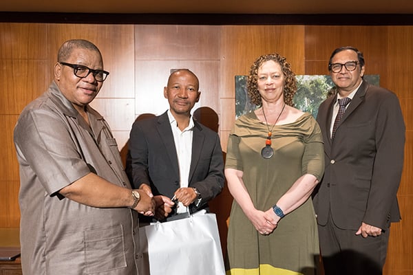 Group picture of Professor Themba Mosia, UP Interim Vice-Chancellor and Principal; Professor Dire Tladi, UP professor of international law and Future Africa's Research Chair in Global Equity in Africa; Professor Loretta Feris, Vice-Principal: Academic; and Professor Sunil Maharaj, Vice-Principal for Research, Innovation and Postgraduate Education. Prof Mosia is handing Prof Tladi a silver gift bag as the two also shake hands.