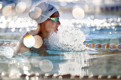 An action side shot of Tatjana Schoenmaker in the pool with a white swimming cap and iridescent swimming goggles.