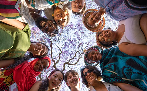 A group of UP students representing various countries stand in a circle and look down on the camera